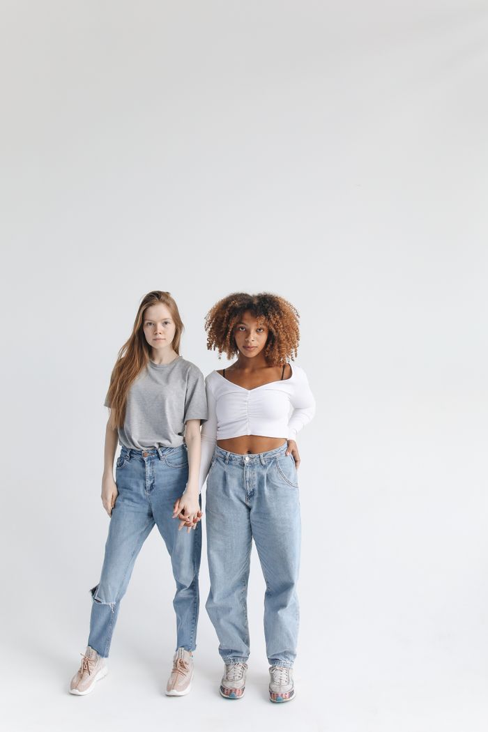 gallery-04 Two young women of different ethnicities standing close in a studio, symbolizing friendship and diversity.