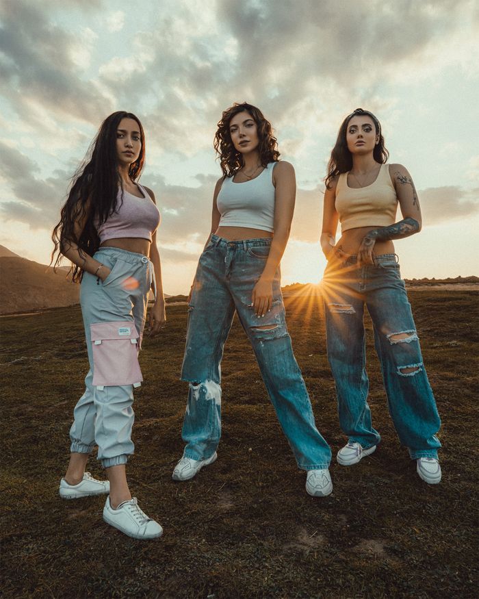 about-img-01 Full body of charming girlfriends in trendy clothes standing in grassy field on hill at sunset